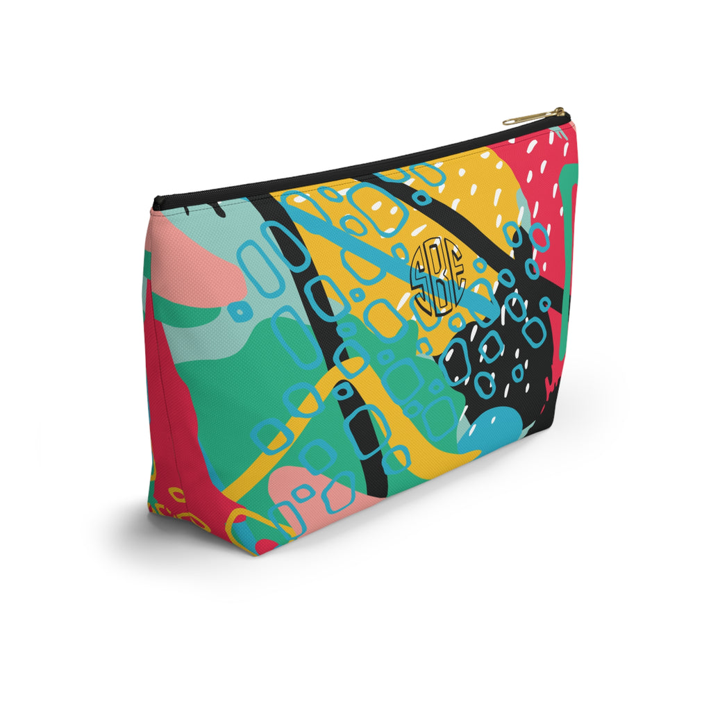 A zippered cosmetic pouch with a colorful abstract pattern featuring yellow, pink, teal, green, black, and white shapes, with a monogram on the back.