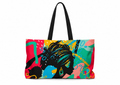 A tote bag with black shoulder straps, featuring a vibrant, multicolored abstract graphic print of a woman's silhouette in black with turquoise, yellow, pink, and teal details, set against a plain white background.