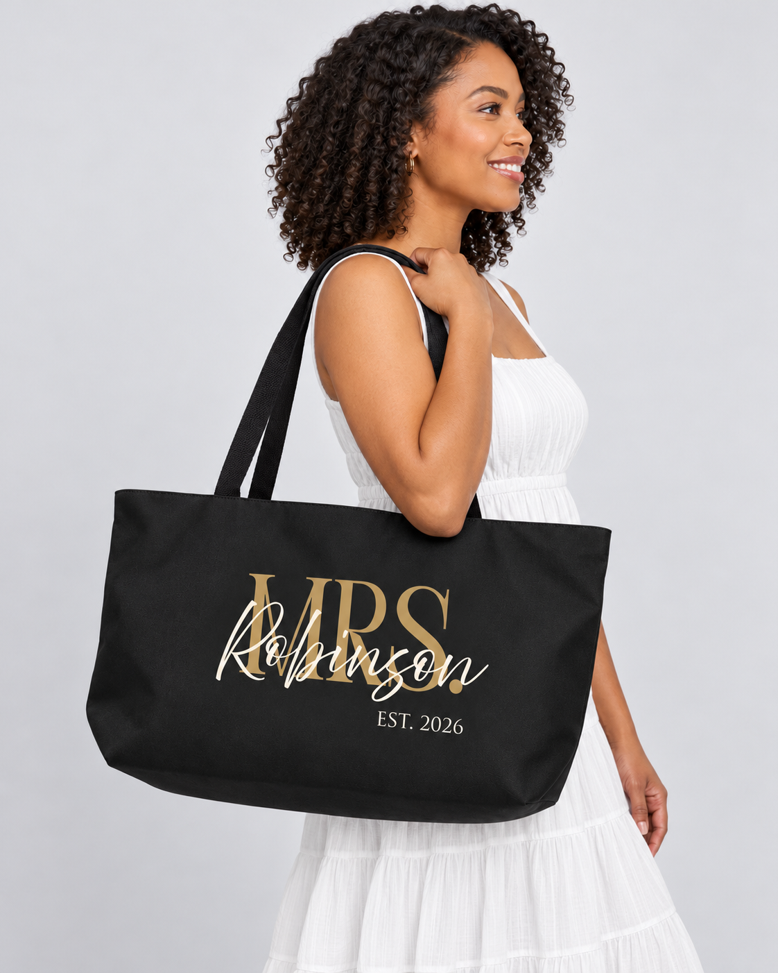 Bride-to-be in a white sundress carrying the black Mrs. Robinson Est. 2026 personalized weekender tote